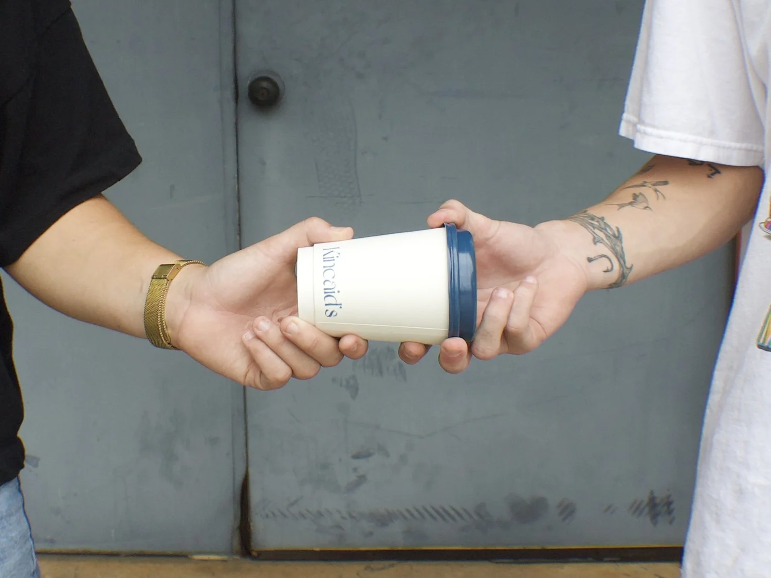 Two hands passing a Kincaid's Coffee cup